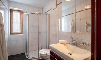 A modern bathroom with a shower cabin, sink, and a toilet. Light tiles and large windows create a friendly atmosphere.