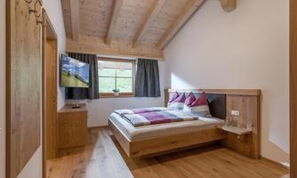 A cozy bedroom with wooden decor and a large window.  
There is a comfortable bed, a television, and a warm, inviting floor.
