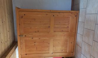 A wooden cabinet with double doors stands in a room. The floor is covered with light tiles.