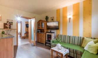 A cozy living room with a green couch and a wooden cabinet. On the wall, there are yellow stripes and a television.