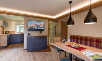 A modern, bright apartment with a dining area and a kitchenette. The space has a cozy atmosphere with wooden details and stylish lamps.