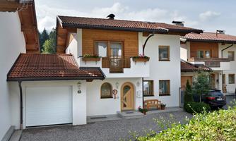 A modern single-family house with a brown gable roof. In front of the house, there is a paved path and a small garden.