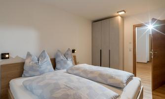 A cozy bedroom with a double bed and large pillows. The room has a modern wardrobe and warm wooden flooring.
