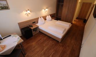 A cozy room with a double bed and wooden floor. There is a table, a chair, and a wardrobe.
