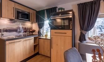 A modern kitchen with wooden cabinets and built-in appliances. Large windows provide bright light and a cozy atmosphere.