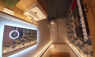 A modern bathroom with an elegant shower and a large mirror. The walls are decorated with a stylish pattern, and there is bright lighting.