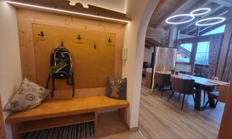 A modern entrance area with a wooden bench and coat rack. In the background, there is an open living and dining area with large windows.
