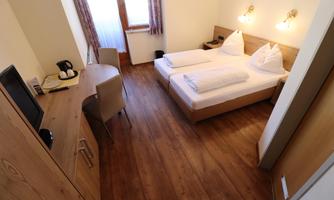 A cozy room with two beds and a desk. The wooden floors and natural light create an inviting atmosphere.