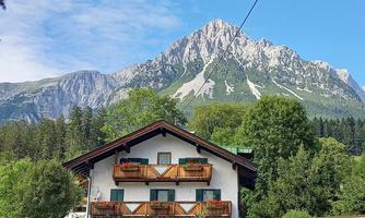 A charming house surrounded by trees and a picturesque mountain landscape. In the background, impressive mountains can be seen under a clear sky.