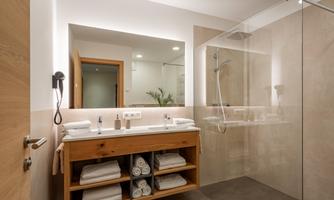 A modern bathroom with a transparent shower and a wooden sink unit. White towels are neatly stacked on a shelf.