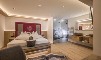 A modern room with a large bed and warm wooden tones. The elegant decor includes a bathroom and decorative elements.