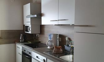 A modern kitchen with white cabinets and a gray countertop. There are various appliances, including a stove and a coffee machine.