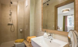 A modern bathroom with a shower and an elegant sink. The pleasant lighting and the wooden mirror create an inviting atmosphere.
