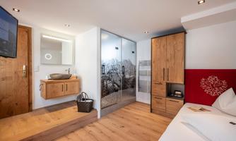 A modern hotel room with wooden flooring and elegant furniture. There is a large window and a built-in shower.