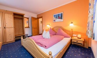 A cozy bedroom with a large bed and pink pillows. The walls are painted orange, and there are wooden cabinets as well as a picture on the wall.