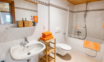A cozy bathroom with a bathtub and a shower. Orange towels and natural wooden shelves create a friendly atmosphere.