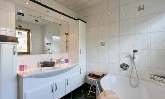 A modern bathroom with a bathtub and a large mirror. The walls are tiled and the fixtures are in white.