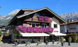 A charming wooden house with colorful flowers on the balcony. Majestic mountains can be seen in the background.