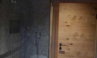 A modern bathroom with a glass shower cabin and a wooden house door. The walls are painted in neutral gray tones.