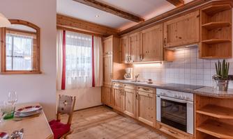 A modern kitchen setup with wooden cabinets and stainless steel appliances. The space is bright and cheerful with large windows and a dining table.