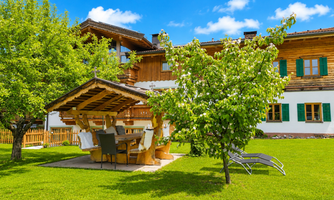 A beautiful wooden house with green shutters and a spacious garden. Under a pergola, a table invites you to relax.