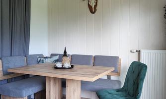A cozy dining area with a wooden table and a bench. A deer antler hangs on the wall, and there is a green chair.