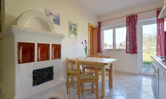 A cozy kitchen with a table and chairs. A traditional fireplace and large windows provide plenty of light.