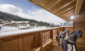A cozy balcony with two chairs and a beautiful view of a snowy landscape. In the background, mountains and cabins can be seen.