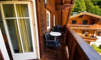 A beautiful balcony with a wooden table and chairs. Trees are visible in the background.