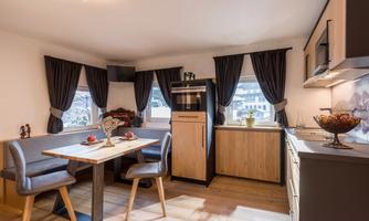 A modern kitchen with a cozy dining area. Large windows and stylish furniture create an inviting atmosphere.