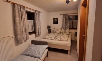 A cozy bedroom with a double bed and a single bed. The walls are painted light, and there are curtains as well as decorative elements.
