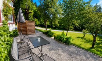 A cozy outdoor area with a table and chairs on gravel.  
Surrounded by trees and a well-maintained lawn.