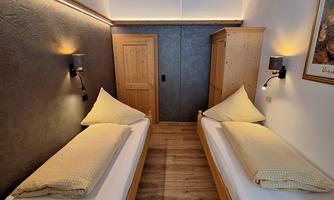 A bright room with two single beds and a wooden ceiling. The walls are in neutral colors, and there is soft lighting.