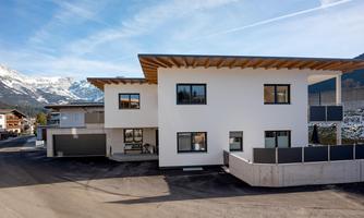 A modern building with a white facade and wood details. Snow-covered mountains are visible in the background.