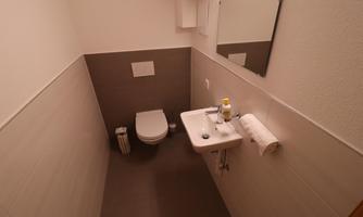 A modern bathroom with a toilet, a sink, and a mirror. The walls are light, and the furnishings are simple and functional.