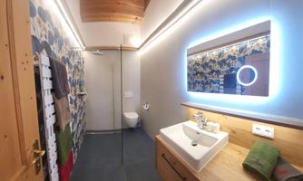 A modern bathroom with a shower and a stylish sink. The walls are partially decorated with a colorful pattern and there is an illuminated mirror.