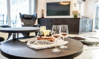 A cozy living room with a wooden table on which two wine glasses and a decoration are placed. In the background, a TV and a comfortable armchair can be seen.