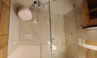 A modern bathroom with a glass cabin and a white toilet. The walls are adorned with elegant marble.
