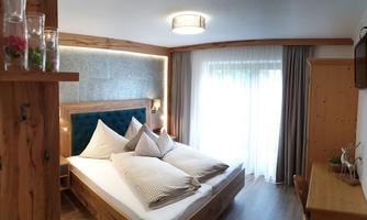 A cozy bedroom with a large bed and bright curtains. The room features wooden details and a desk.