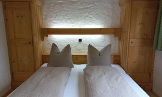 A cozy bedroom with a double bed and wooden wardrobes. The pillows have a distinctive shape and the light is softly placed behind the bed.