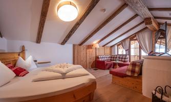 A cozy room with wooden beams and a large skylight. There is a double bed and a lounge area with a comfortable couch.