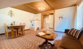 A cozy living room with a dining table and chairs. The room has a modern, bright style with wooden elements and a comfortable sofa.