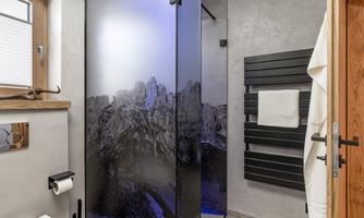A modern bathroom with a glass shower and a mountain motif. The walls are in neutral tones, and there is a metal towel holder.