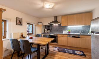 A modern kitchen with a dining table and chairs. The wooden surfaces and gray accents give it a cozy look.
