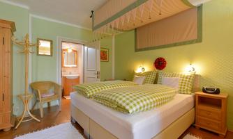 A cozy bedroom with a large bed and green walls. The room is friendly and bright with wooden furniture and a carpet.