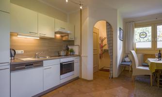 A modern kitchen with white cabinets and a stove. Next to the kitchen are a dining table and a cozy area.