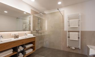 A modern bathroom with a shower and bright tiles. There is a wooden cabinet with clean towels and a cozy atmosphere.