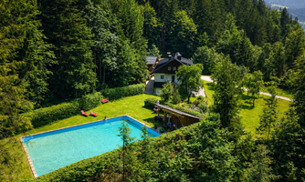 An idyllic house amidst trees with a blue swimming pool. The green space around the house invites you to relax and linger.