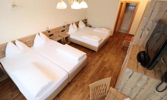 A bright room with two single beds and wooden furniture. There is a television and a beautiful wooden floor.