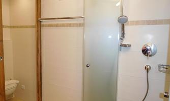 A modern bathroom with a shower and a toilet. The walls are light tiled and the furnishings are simple and functional.